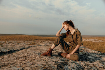 Lonely woman contemplating life on top of a rock in the middle of a field as a concept of solitude...