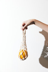 Person holding an orange in a white net bag against a white wall