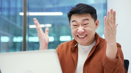 Happy excited asian businessman received great news on laptop while sitting at workplace in business office. Smiling shocked surprised entrepreneur reads a positive good message on computer. Close up