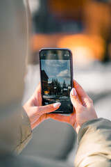 Person holding smartphone while capturing scenic winter landscape in a vibrant city
