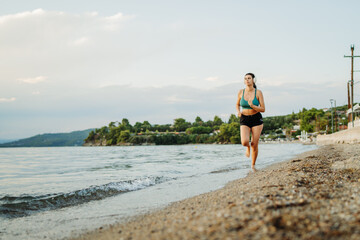 Fototapeta premium Young woman running or jogging on the beach at sunset 