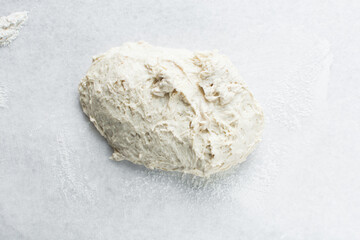 Overhead view of high hydration dough being shaped on a white granite countertop, top view of homemade bread dough on white countertop, process of making artisan bread