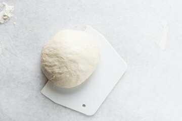 Overhead view of high hydration dough being shaped on a white granite countertop, top view of homemade bread dough on white countertop, process of making artisan bread