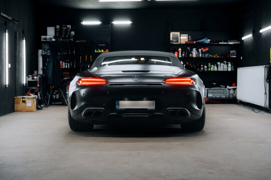 Rear view of a Mercedes AMG GT C Roadster in a detailing studio, showcasing its sleek matte black finish and aggressive LED taillights. Ideal for marketing, advertisements, and automotive promotions.