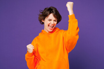 Young smiling happy Caucasian woman she wear orange hoody casual clothes doing winner gesture...