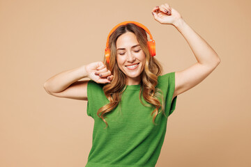 Young smiling happy woman she wear green t-shirt casual clothes listen to music in headphones raise...