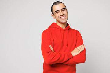 Young smiling happy cheerful middle eastern man he wear red hoody casual clothes hold hands crossed folded looking camera isolated on plain solid white background studio portrait. Lifestyle concept.