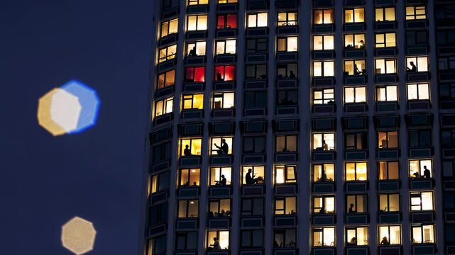 Nighttime urban panorama revealing illuminated skyscraper windows, showcasing silhouetted residents within high rise apartment spaces, capturing metropolitan living dynamics