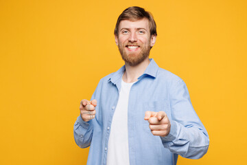 Young smiling confident leader man he wear blue shirt white t-shirt casual clothes point index finger camera on you motivating encourage isolated on plain yellow background studio. Lifestyle concept.
