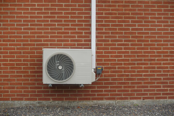 Air-source heat pump's external heat exchanger, mounted on red brick wall with white conduit and...