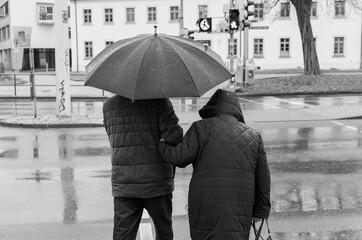 Pensioner couple walking in the rain at a traffic light in the city of black and white photography...