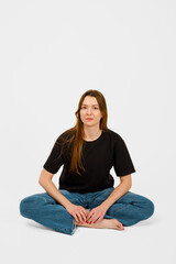 Fototapeta premium Woman sitting cross-legged on floor in simple attire with neutral background