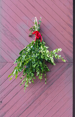 Green foliage bundle with red ribbon on wooden door