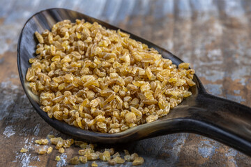 Bulgur wheat grains in a wooden spoon resting on a rustic table