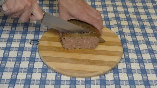 to cut into pate with a knife, man cutting pieces of baked pate on a wooden kitchen board