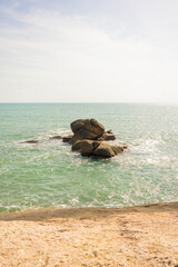 A landscape of beautiful rocks around the ocean. Sunlight reflects off the water, creating a shimmering effect. The scene conveys a sense of calmness: soft waves rolling over the rocks.