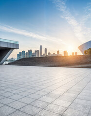 Fototapeta premium A modern urban landscape featuring a spacious, open-air tiled plaza with a scenic view of the city skyline at sunrise or sunset.