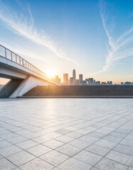 A modern urban landscape featuring a spacious, open-air tiled plaza with a scenic view of the city skyline at sunrise or sunset.