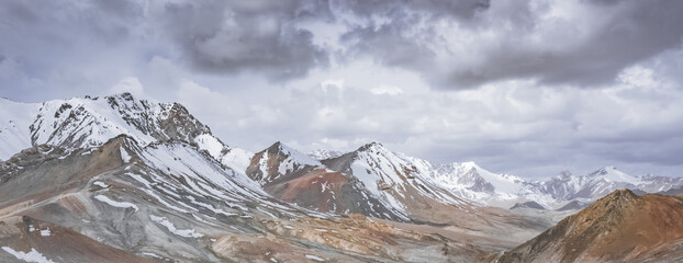 Panorama of mountain range with rocks, stones and snow, landscape in the highlands of Tien Shan in Pamir in Tajikistan, cloudy cloudy landscape for background