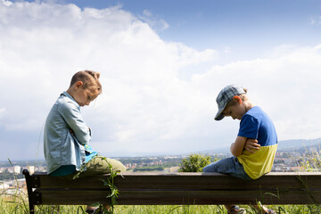 Upset brothers or friends sulk, sitting at a distance from one another and not talking. children...