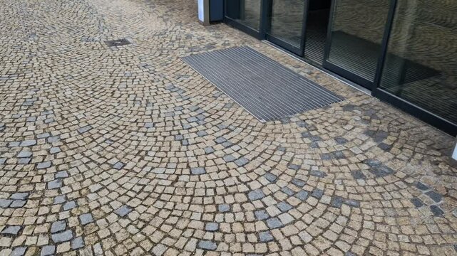industrial mat cleaning zones at the entrance to the building. A black plastic-metal mat in the shape of an arch or half-circle lies on the limestone mosaic tiles, granite, cube, cobblestone, office