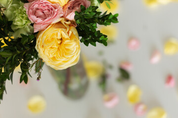 A close-up shot from above of yellow and pink flowers in a vase and petals lying nearby. Focus on flowers