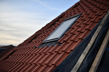 Spiegelndes Dachfenster in neuem Hausdach mit roten Dachziegeln vor hellblauem Himmel