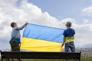 large Ukrainian flag in the hands of two boys against the sky. National symbol of independence....