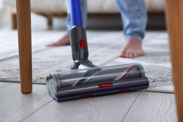 Man cleaning floor with cordless vacuum cleaner at home, closeup