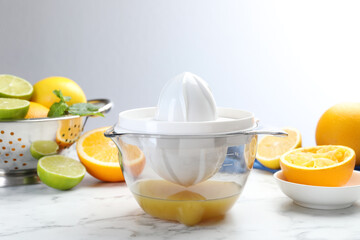 Plastic juicer and different citrus fruits on white marble table, closeup