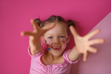 A girl with the details of colored puzzles on her face extends a helping hand. A concept photo as a sign of support for people with autism