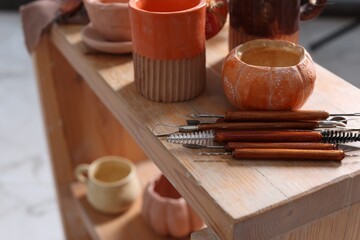Set of different crafting tools and pottery on wooden shelf indoors, closeup