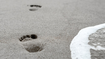 footprints in the sand on the beach near the surf