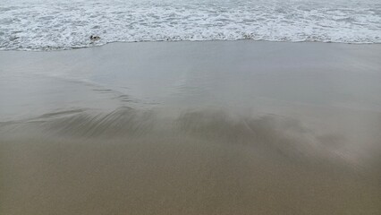 Close-up view of gentle waves lapping against the sandy shore, perfect for beach and relaxation themes