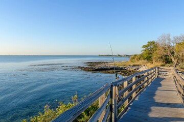 Fototapeta premium Scenic Coastal Boardwalk Overlooking Calm Waters Under Clear Blue Sky at Sunset