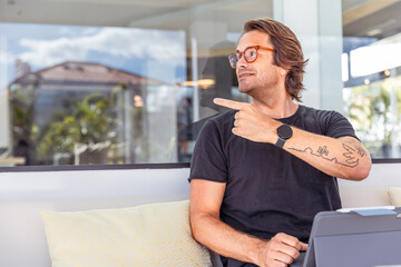 A hipster man with a tattoo on his arm points to the left, copy space working space photo