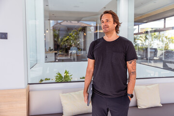 Fototapeta premium A businessman in a black shirt stands in front of a window with a tablet in his hand