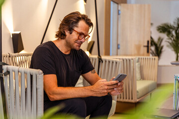 A man is sitting on a couch and looking at his cell phone