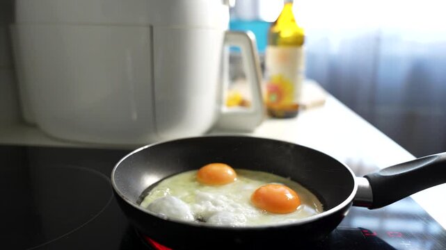 A pan with two eggs and a bottle of oil on a counter. The pan is on a stove