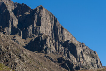 Kabardino-Balkaria. El-Tyubu. Rocky mountains with trees growing on their slopes glow in morning sun. Close-up. Chegem Gorge. Unique rocky ridge with steep cliffs against blue autumn sky.