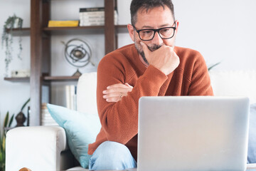 Concentrated adult businessman in eyewear looking at laptop screen, web surfing information in...