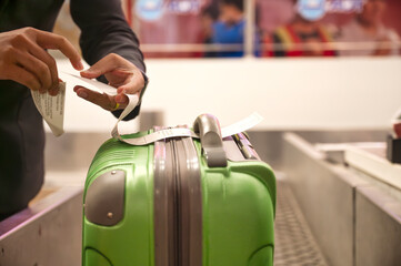 Close-up of a green suitcase being labeled by an airport staff member at a check-in counter, representing travel preparation and airline baggage handling
