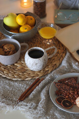 Books, e-reader, tea, orange juice, fruit, snacks, yarn, blanket and lit candles on the table. Autumn or winter hygge at home. Selective focus.