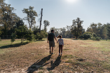 A father and daughter walk hand in hand through a park, enjoying quality time and the beauty of the...