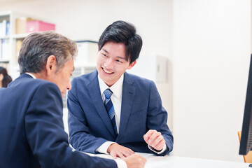 窓口で高齢者の来客の対応をする男性