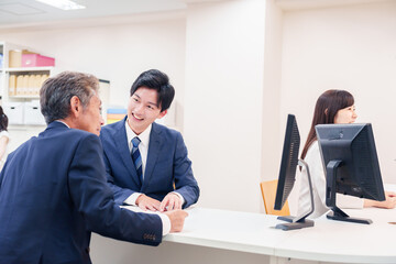 窓口で高齢者の来客の対応をする男性