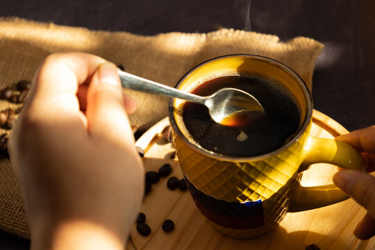 Female hand stirring with a spoon hot coffee in a yellow cup with Colombia flag in the morning