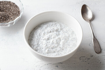 Healthy Chia Seed Pudding in White Bowl with Spoon and Dry Chia Seeds on Light Background