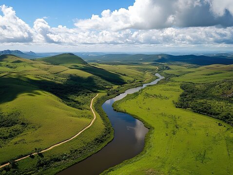 Aerial view of a winding river through green hills with a cloudy sky above
