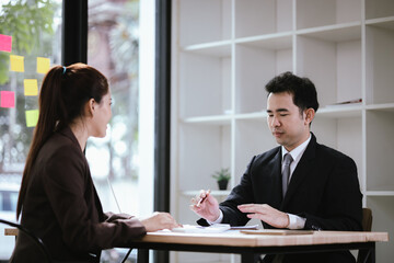 Two Asian businessmen in modern office having professional conversation using laptop and mobile phone. Communication, strategy and corporate success.